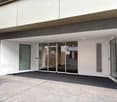 Modern building entrance with glass sliding doors, white walls, and a covered walkway.