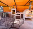 Outdoor patio with a wooden roof, a round wooden oven, a grill, a sink, and a dining area with a table and chairs.