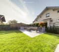 Well-maintained garden with a lawn, patio area, lounge chairs, and a small seating area near the house.