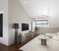 Modern living room with white walls, wooden flooring, a large sectional sofa, a round coffee table, a floor lamp, a TV mounted on the wall, and decorative artwork.