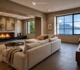Modern living room with large windows offering a scenic mountain and lake view, a beige sectional sofa, a black coffee table, a fireplace, and decorative lamps.