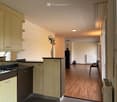 modern kitchen with island, wooden cabinetry, black countertops, dishwasher, sink, faucet, built-in appliances, vase with plants, chair, radiator