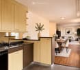 Open-concept kitchen and living area with light wood cabinets, stainless steel appliances, a dining table with chairs, a sofa, and decorative items.