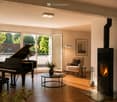 Modern living room with hardwood floors, large windows, grand piano, fireplace, sofa, coffee table, and floor lamp.