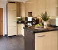 Modern kitchen with light wood cabinets, granite countertop, stainless steel appliances, and decorative items including a vase and fruit bowl.