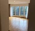 Empty room with wooden flooring, large windows with white frames, and light-colored walls.
