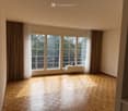 Empty room with wooden parquet flooring, large windows with curtains, and a radiator beneath the windows.