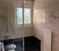 Bathroom with tiled walls, a toilet, a sink, a shower area with a glass door, and a radiator.