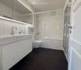 modern bathroom with white tiles, black floor, white vanity, silver faucet, white toilet, bathtub, towel rack