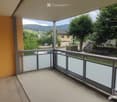 Balcony with modern glass balustrade, overlooking a green landscape with trees and distant mountains.