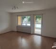 Empty room with wooden flooring, white walls, large windows, and a radiator. No furniture or equipment present.