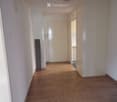 Empty hallway with wooden flooring, white walls, and a closed door leading to another room.