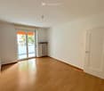 Empty room with light wooden flooring, white walls, a sliding glass door leading to a balcony, and a radiator on the wall.