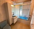 Bathroom with a toilet, sink, bathtub, and a mirror. The room features tiled walls and a wooden ceiling.