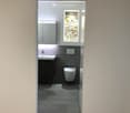 Modern bathroom with a white sink, dark cabinet, toilet, and a vase with yellow flowers on a window sill.