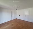 Empty room with white walls, wooden herringbone flooring, and a decorative ceiling light fixture. Three white doors are visible.