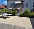 Garden area with a table tennis table, white fence, and surrounding greenery near a two-story house with balconies.