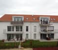 Two-story white house with red-tiled roof, multiple balconies, and a well-maintained garden area.