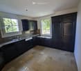 Empty kitchen with dark wooden cabinets, a tiled floor, and two windows letting in natural light.