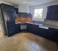 Modern kitchen with dark cabinets, granite countertops, a stainless steel sink, and a refrigerator. The floor is tiled in a herringbone pattern.