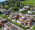 Aerial view of a residential area with modern houses, solar panels on rooftops, well-maintained gardens, and a scenic green landscape in the background.