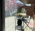 Balcony with a small table and two chairs, overlooking a garden with blooming trees and a pathway.
