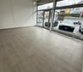 Empty room with light-colored tiled flooring and large glass windows showing a parking area outside.