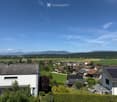 A rural village with scattered houses, green fields, and distant mountains under a clear blue sky.
