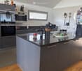 Modern kitchen with grey cabinets, granite countertop, stainless steel appliances, and various kitchen items including a bottle, bowl, and knife block.