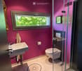 Modern bathroom with pink walls, a white sink, toilet, glass-enclosed shower, and a round rug on the floor.