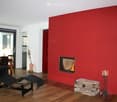 Modern living room with a red accent wall, fireplace, black leather sofa, dining table, and chairs.