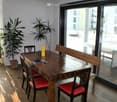 Bright, modern dining area with wooden table, red chairs, bench seating, and potted plants near large windows offering a city view.