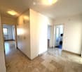 Empty hallway with white walls, marble flooring, built-in white closet, and recessed lighting. Three doors lead to other rooms.