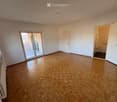 Empty room with wooden parquet flooring, white walls, and large windows. Features a sliding glass door leading to a balcony and an open doorway to a bathroom.