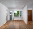 Empty room with wooden flooring, white walls, large window with view, and a radiator below it.