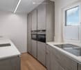 Modern kitchen with white countertops, stainless steel sink, built-in oven, and grey cabinets.