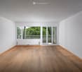 Empty room with wooden flooring, white walls, large windows, and a sliding glass door leading to a balcony.