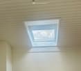 Empty room with light-colored wooden flooring, white walls, and a skylight window. A single light fixture hangs from the ceiling.