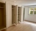 White cupboards, empty shelves, window, power outlets, wooden floor