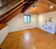 Empty attic space with wooden flooring, white walls, exposed wooden beams, and a small window. A small sink is installed in one corner.