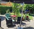 A well-maintained garden patio with outdoor furniture including tables, chairs, and potted plants, surrounded by greenery and a hedge.