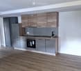 Modern kitchen with wooden and grey cabinets, stainless steel appliances, and a wooden floor.