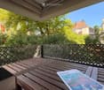 Balcony with wooden table and chairs, featuring a lattice fence and a view of greenery and neighboring buildings.