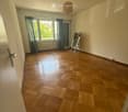 Empty room with wooden parquet flooring, large window with curtains, and a simple hanging light fixture.