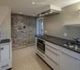 Modern kitchen with white cabinets, black countertop, stainless steel sink and faucet, built-in oven, and a range hood. Exposed stone wall adds texture.