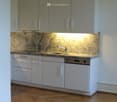 Modern kitchen with white cabinets, granite countertop, and wooden flooring.