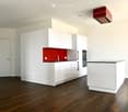 Modern kitchen with white cabinets, a red backsplash, a central island, and a dark wooden floor.