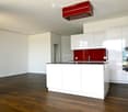 Modern kitchen with white cabinets, dark wooden floor, red backsplash, and stainless steel appliances.