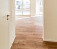 Empty hallway with light wooden flooring, white walls, and a sliding glass door leading outside.