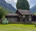 Wooden alpine house, stone chimney, wooden fence, green hay bales, mountains, grass field